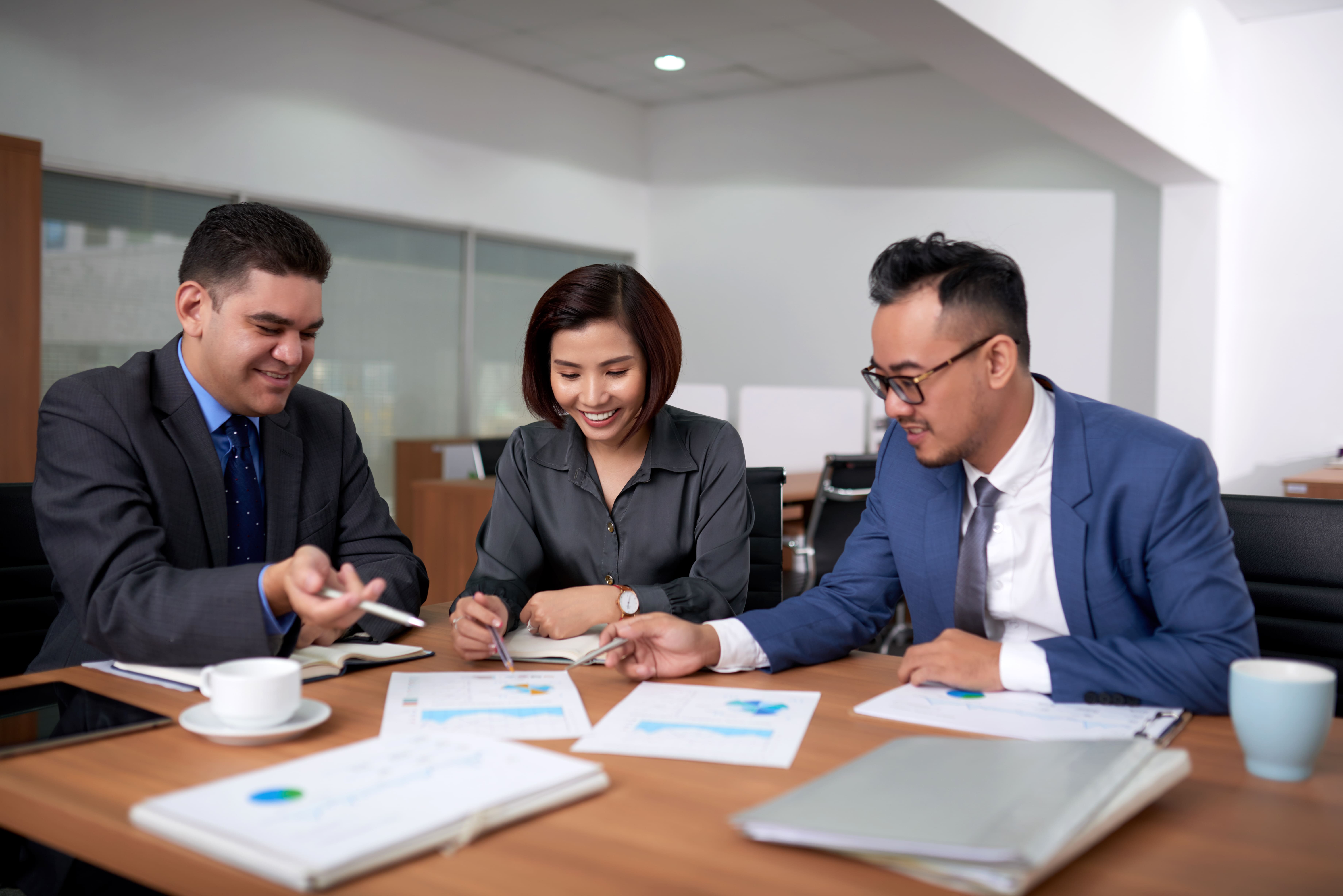multiethnic-male-female-colleagues-sitting-office-discussing-charts-meeting